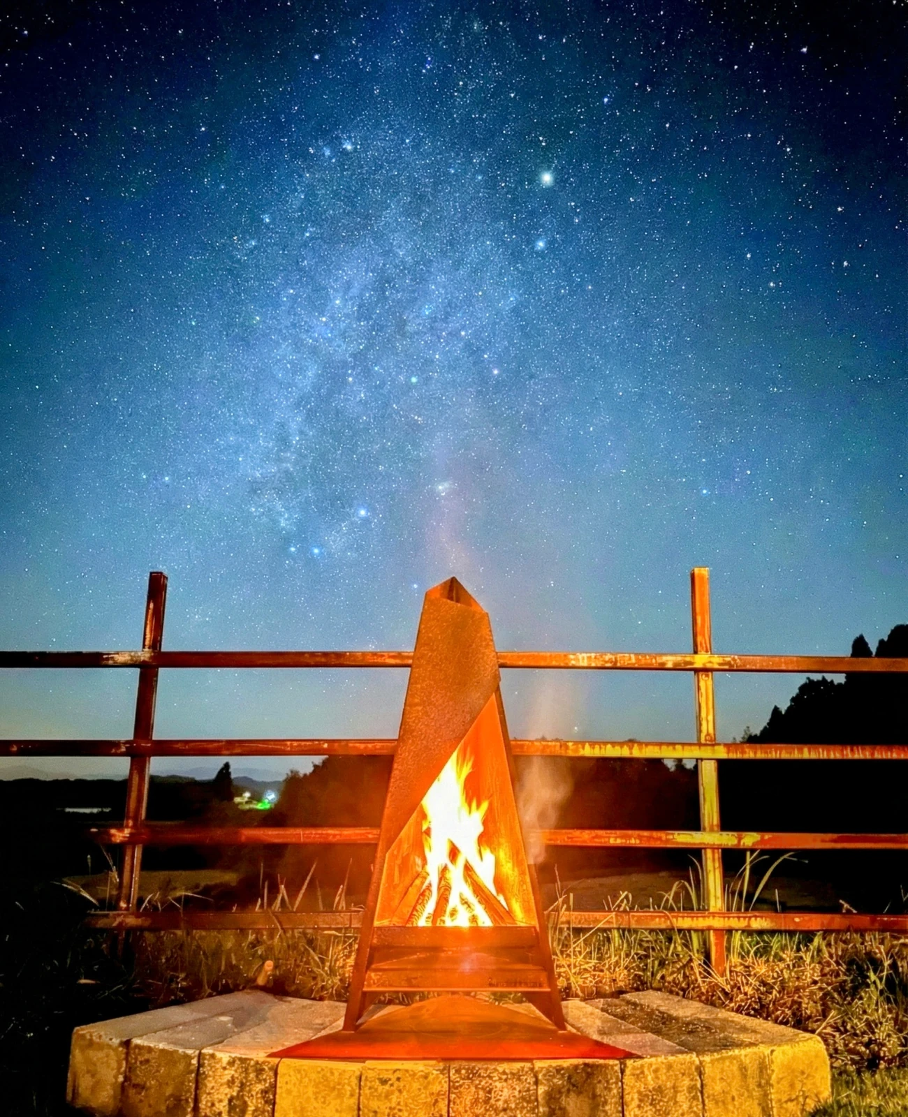 天の川が広がる星空の下、庭の焚き火台に上がる炎